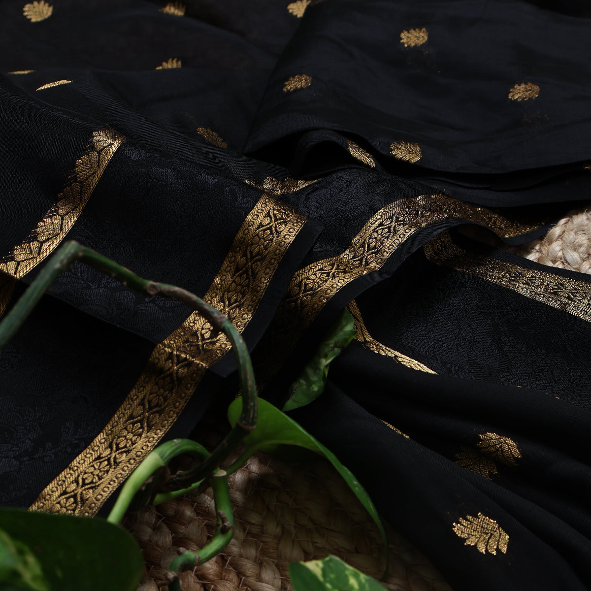 Black saree with gold embroidery and patterns, partially covering a woven surface.