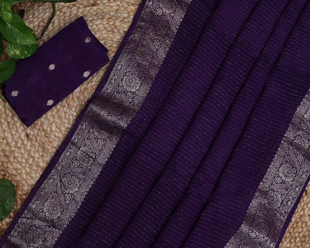 Purple saree with silver pattern on a textured surface with green leaves.
