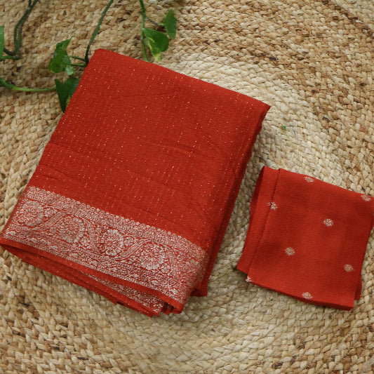 Red saree with a patterned border and a small red pouch on a woven surface.